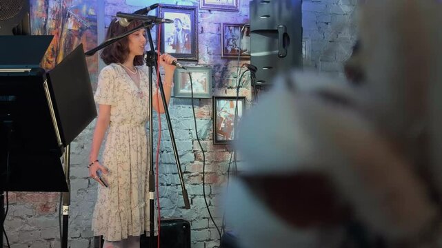 Emotional Young Female Poetess Reciting Poetry with Microphone on Stage inside Retro Club Interior Peeping POV Shot through Massive Blurred Foreground Bokeh Authentically Handheld Footage