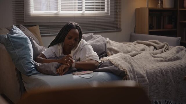 African American young adult woman waking up in bed, checking smartwatch and burying face in pillow. Video is suitable for mental health awareness and digital burnout campaigns