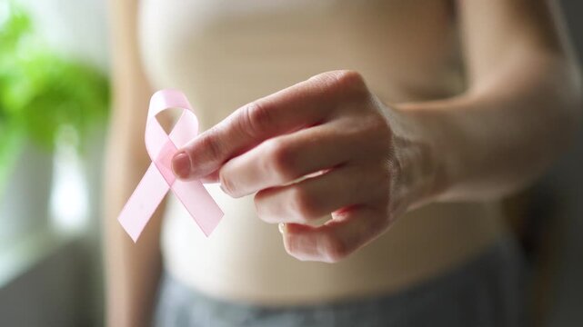 Close-up of female hand holding pink satin ribbon, symbolizing support for breast cancer awareness, medical care, and self-examination.