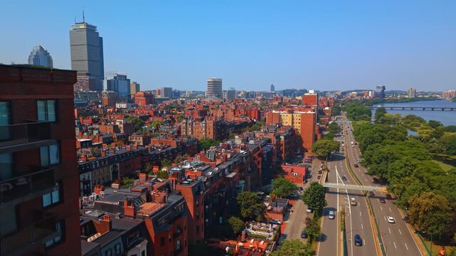 Approaching the rows of red brick buildings in Back Bay neighborhood of Boston, Massachusetts. Drone footage over the road along the lush greenery on the river waterfront.