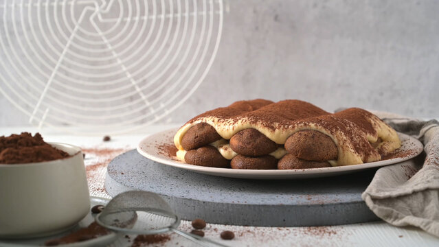 Delicious homemade tiramisu cake served on a plate with cocoa powder and coffee beans on a kitchen table