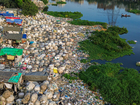 Aerial view of the Buriganga river canal bank covered in plastic waste and makeshift shelters near water hyacinth in Dhaka, Dhaka Division, Bangladesh.