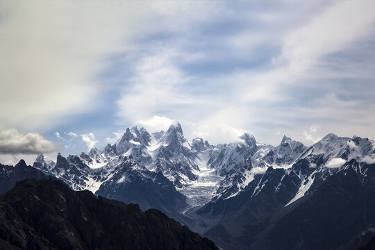 Aerial view of Uli Biaho Peak with snow-capped mountain ranges, glaciers, and rocky slopes under a cloudy sky in Skardu, Pakistan.
