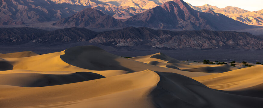 Aerial view of Death Valley sand dunes with golden light, dramatic shadows, and rugged mountains in the background in Inyo County, California, United States.