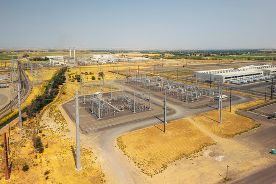 Aerial view of a data center facility with an adjacent electrical substation, power lines, and industrial buildings in a dry landscape in Umatilla, Oregon, United States.