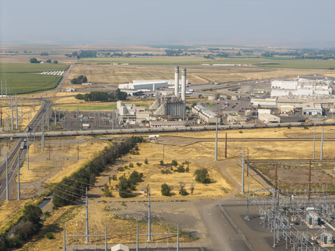 Aerial view of the Hermiston Generating Project power plant with tall smokestacks, electrical substation, and surrounding dry fields in the landscape of Hermiston, Oregon, United States.
