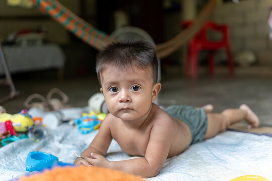 Cute mexican baby looking at camera while playing on a blanket inside a rural house
