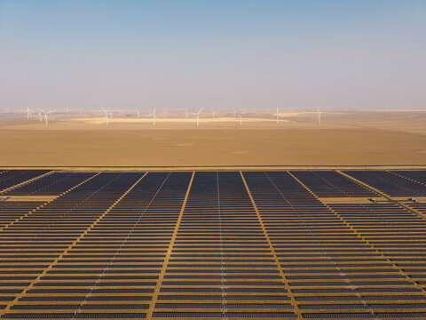 Aerial view of Arlington solar farm with rows of photovoltaic panels and wind turbines in the background under a clear sky in Arlington, Oregon, United States.