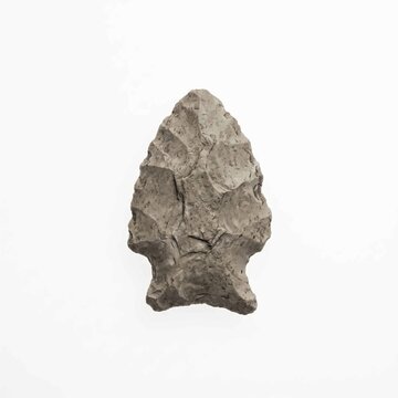Ancient stone arrowhead crafted from chipped grey flint displays sharp jagged edges isolated against a clean plain white studio background