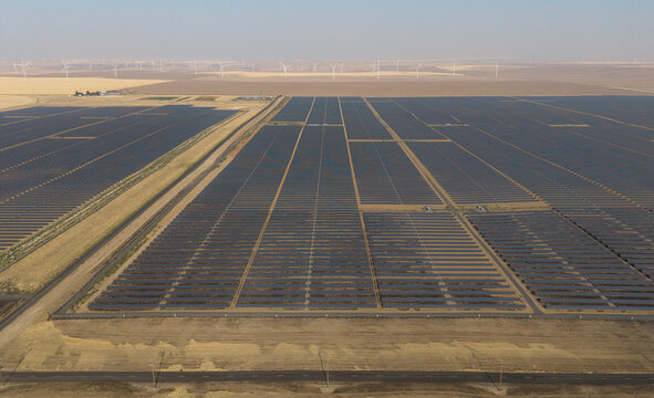 Aerial view of the Arlington solar farm with rows of photovoltaic panels stretching across the landscape, surrounded by dry fields and wind turbines in Arlington, Oregon, United States.