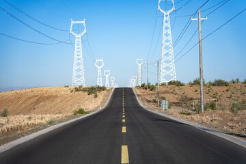 Naklejka premium power transmission towers and rural asphalt road under blue sky