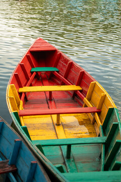 View of a colorful wooden boat with red, yellow, and green painted planks floating on the water in Pokhara, Gandaki Province, Nepal.
