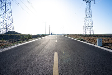 Naklejka premium straight asphalt road stretching towards the horizon under bright sunlight with high voltage power towers on both sides