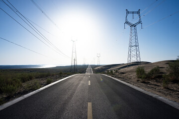 Naklejka premium Desert highway stretching towards the horizon under bright sunlight with high voltage transmission towers