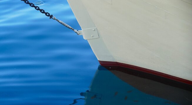 White wooden boat on the sea in harbor with reflection in water, sea transportation and nautical boat background