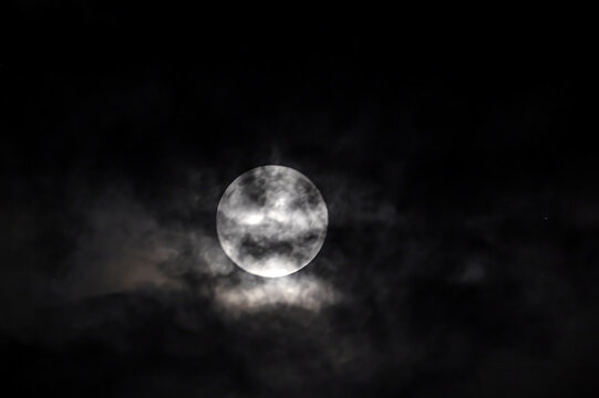 View of the full moon partially obscured by dark, wispy clouds in the night sky over Jahanian, Pakistan.