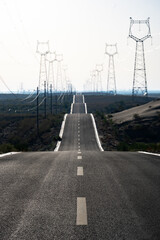 High voltage transmission towers extending along the desert highway road © zhu difeng