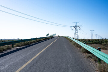 Naklejka premium Empty asphalt road with green guardrails and high voltage power towers under blue sky