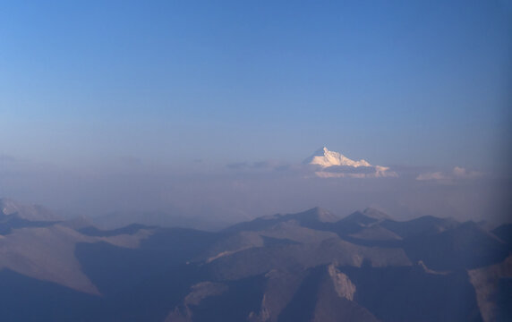 View of Rakaposhi peak rising above a hazy mountain range under a clear blue sky in Pakistan.