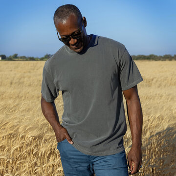 Blank washed grey t-shirt mockup on black man in wheat field at sunset, front view with copy space