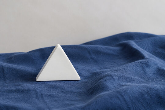 Single white equilateral triangle object on deep blue linen, calm still life for editorial concept