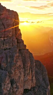 Aerial side reveal flight across dramatic Dolomite cliffs at sunset, unveiling majestic alpine peaks under glowing evening light. Cinematic drone footage with panoramic mountain scenery in Italy.