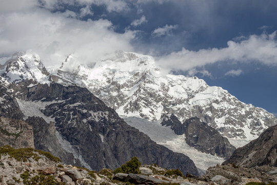 View of Nanga Parbat mountain peak with snow-covered slopes, glaciers, and rocky terrain under a blue sky with clouds in Chilas, Pakistan.