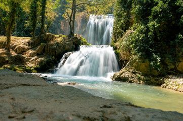 A waterfall cascades over rock ledges surrounded by greenery in the Monasterio de Piedra natural park in Aragon Spain a soft long exposure of silky white water and a turquoise pool. © Oksana