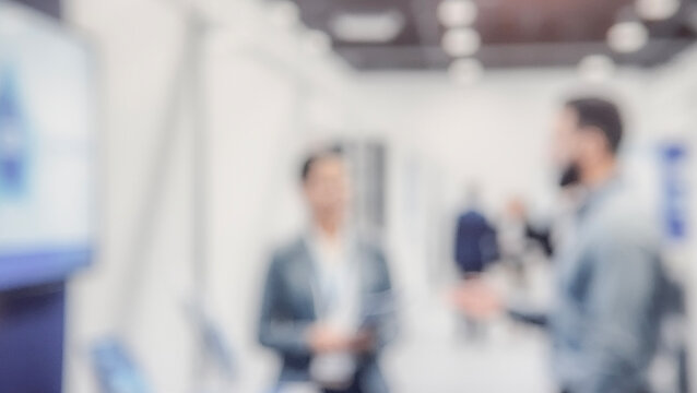 A blurred image of two individuals engaged in a conversation at a trade show or conference, surrounded by a professional environment.