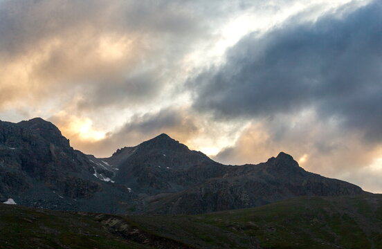 View of the dramatic rocky peaks and grassy slopes of Burzil Pass under a cloudy sunset sky in Astore, Gilgit Baltistan, Pakistan.