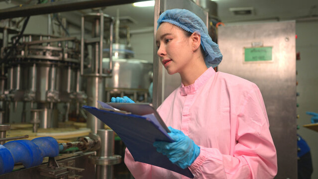 Quality control worker reviewing production data on clipboard during bottled beverage filling process in factory