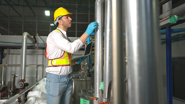 Engineer using laptop to monitor chia seed fruit juice production machinery in automated beverage factory system