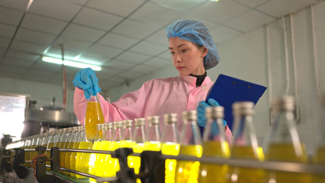 Female worker inspecting bottled beverage on production line in factory environment