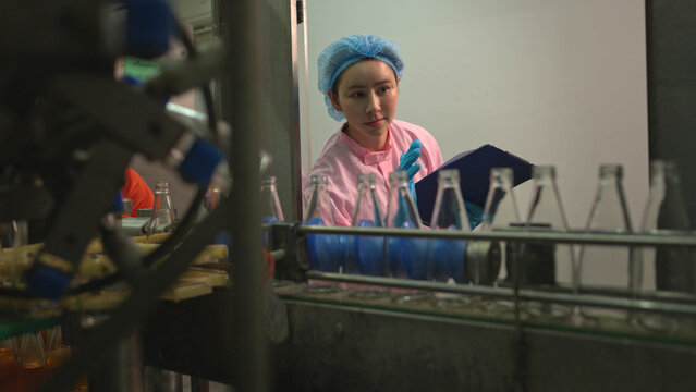 Quality control worker reviewing production data on clipboard during bottled beverage filling process in factory