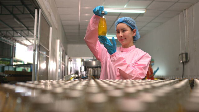 Female worker inspecting bottled beverage on production line in factory environment