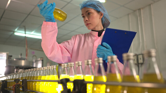 Female worker inspecting bottled beverage on production line in factory environment