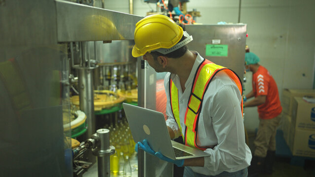 Engineer using laptop to monitor chia seed fruit juice production machinery in automated beverage factory system