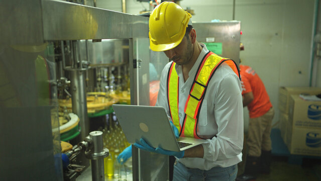 Engineer using laptop to monitor chia seed fruit juice production machinery in automated beverage factory system