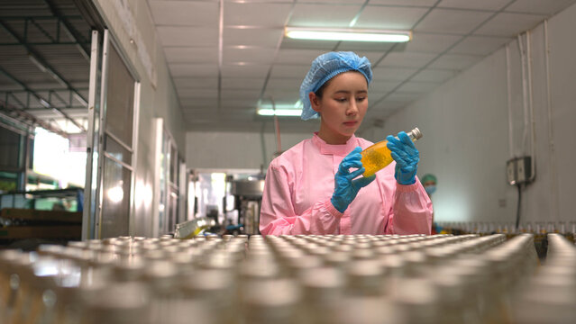 Female worker inspecting bottled beverage on production line in factory environment