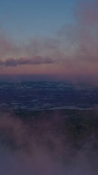 Smooth flight over snow covered forests, rolling hills, and low clouds at sunrise. Peaceful alpine landscape with soft sunset light. Vertical aspect ratio.