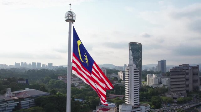 National flag of Malaysia waving proudly on tall flagpole in Kuala Lumpur city center.