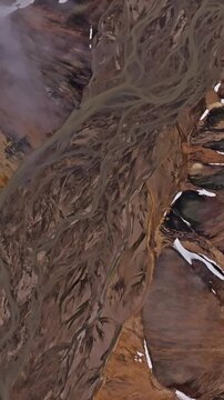 Cinematic rotating aerial ascent above braided glacial rivers in Iceland&rsquo;s Rainbow Mountains revealing colorful rhyolite slopes intricate meltwater channels and dramatic Highland landscapes.