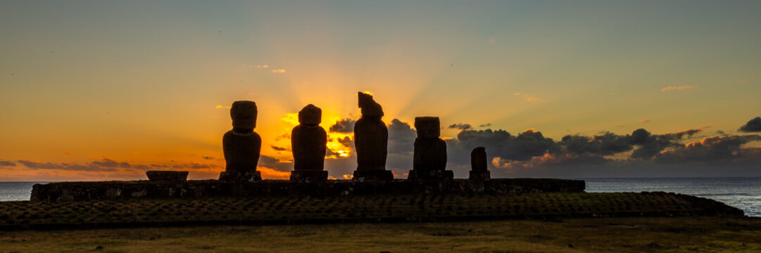 Moais Tahai Archaeological Complex. View of the iconic Moai statues silhouetted against a vibrant sunset over the Pacific Ocean on Easter Island, Valparaiso, Chile.