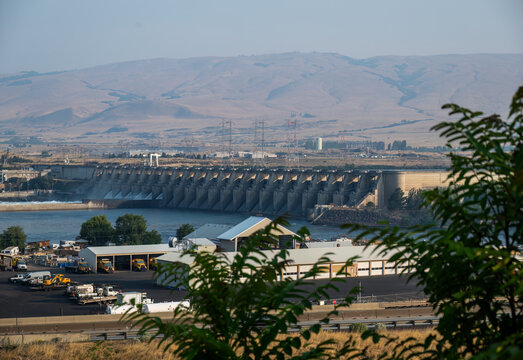 View of The Dalles Dam spanning the Columbia River with industrial facilities, service vehicles, and arid hills in the background The Dalles, Oregon, United States.