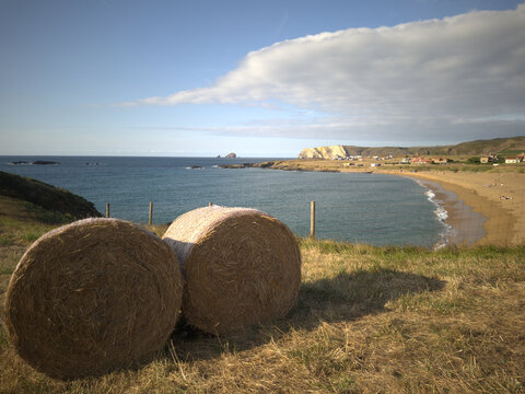 Rollos de paja redondos en un acantilado verde con vistas a una playa de arena dorada y al mar Cant&aacute;brico en Asturias