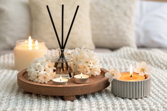 Cozy home interior with burning candles and a reed diffuser on a wooden tray with flowers on a soft knit blanket
