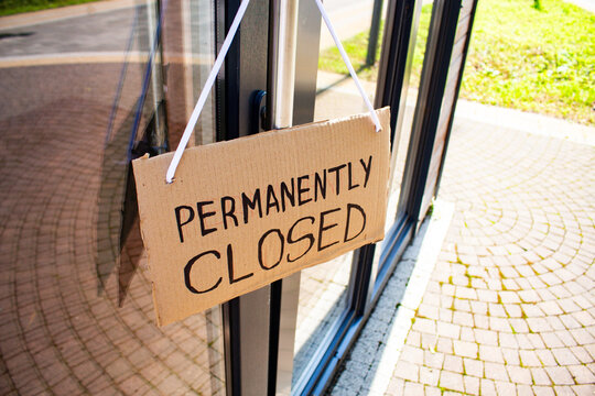 PERMANENTLY CLOSED sign hanging on small shop door. Small business shutting down due to financial crisis. Local business unable to survive economic pressure