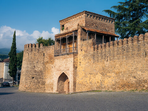 View of the historic Batonis Tsikhe fortress with its stone walls, pointed arch entrance, and wooden balcony under a clear blue sky in Telavi, Kakheti, Georgia.