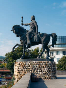 View of the bronze equestrian statue of King Erekle II on a stone pedestal, set against a clear blue sky with a modern building in the background in Telavi, Kakheti, Georgia.