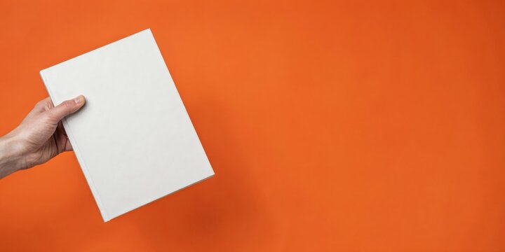Hand holding a blank white book cover on orange background